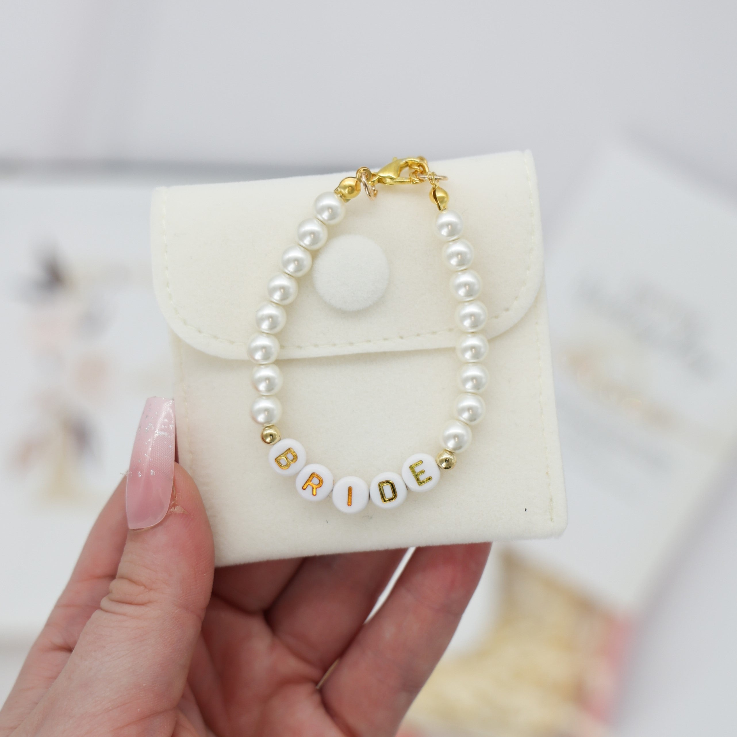 Beaded bracelet with BRIDE letter-beads and faux pearls on a pouch, part of A Little Gift for the Bride set, held by a manicured hand.