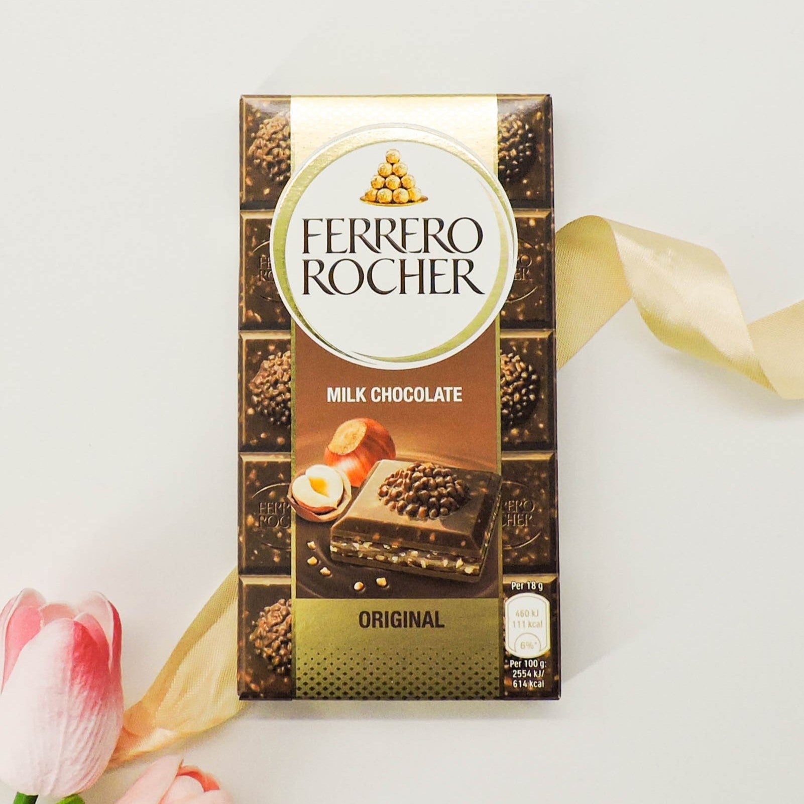 Ferrero Rocher Milk Chocolate Bar with crunchy hazelnuts, depicted alongside a rose petal and yellow ribbon, emphasizing its luxurious appeal.