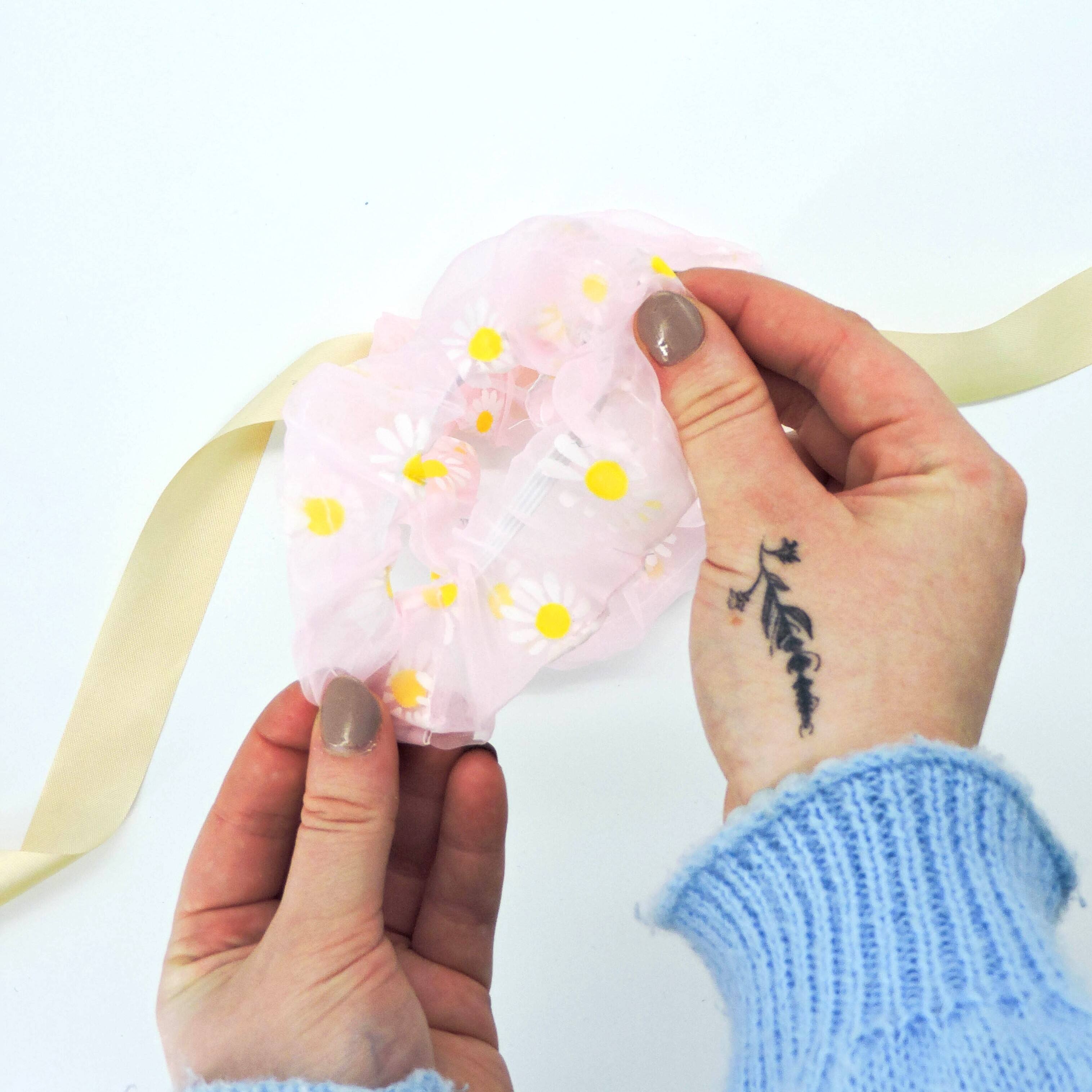 Hand holding Daisy Hair Scrunchie - Pink with a floral design, showcasing its soft, lightweight fabric perfect for hair styling or as a wrist accessory.