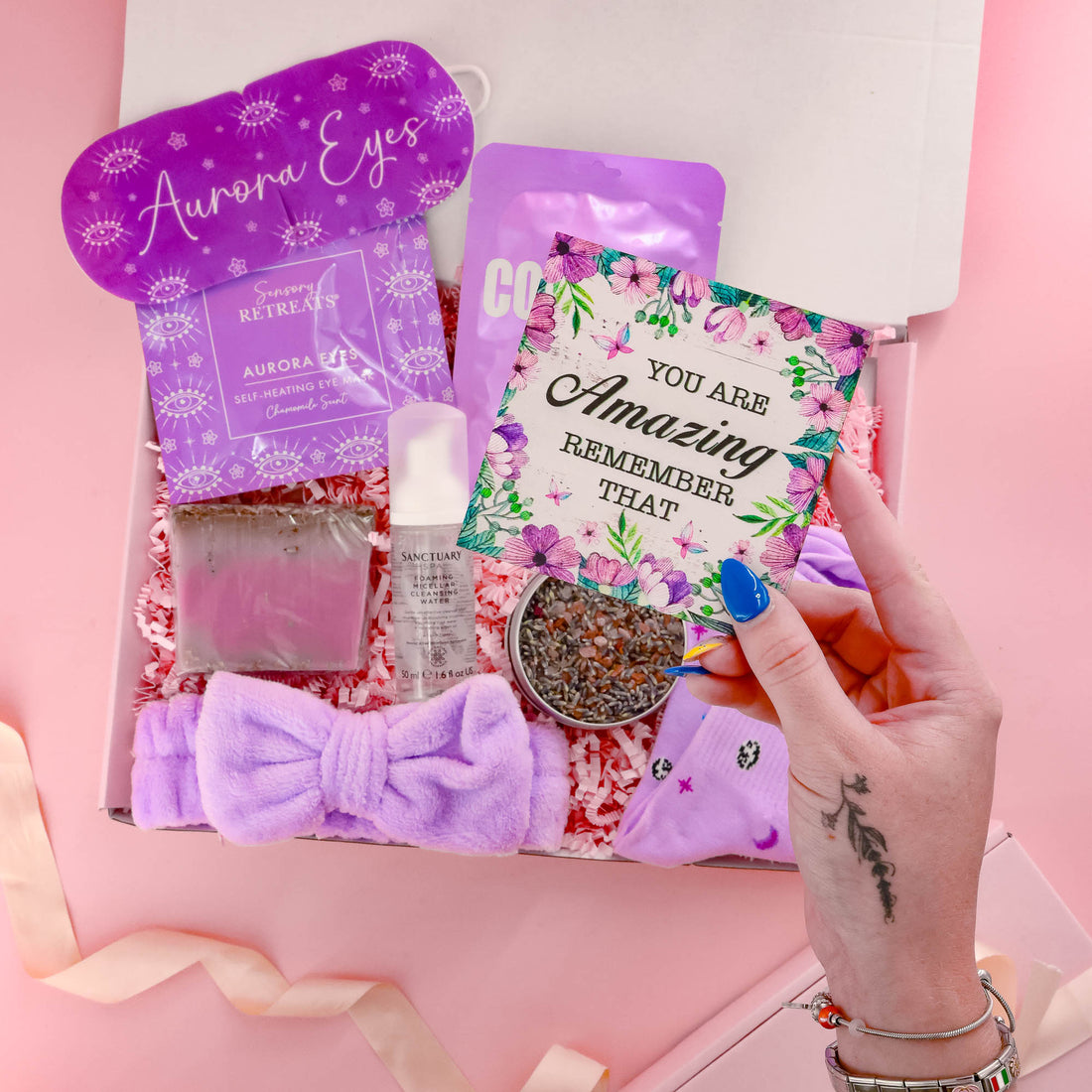 Thoughtful gift for her featuring selfcare essentials like collagen mask, lavender bath soak, bow headband, cleansing water and a positive affirmation card.