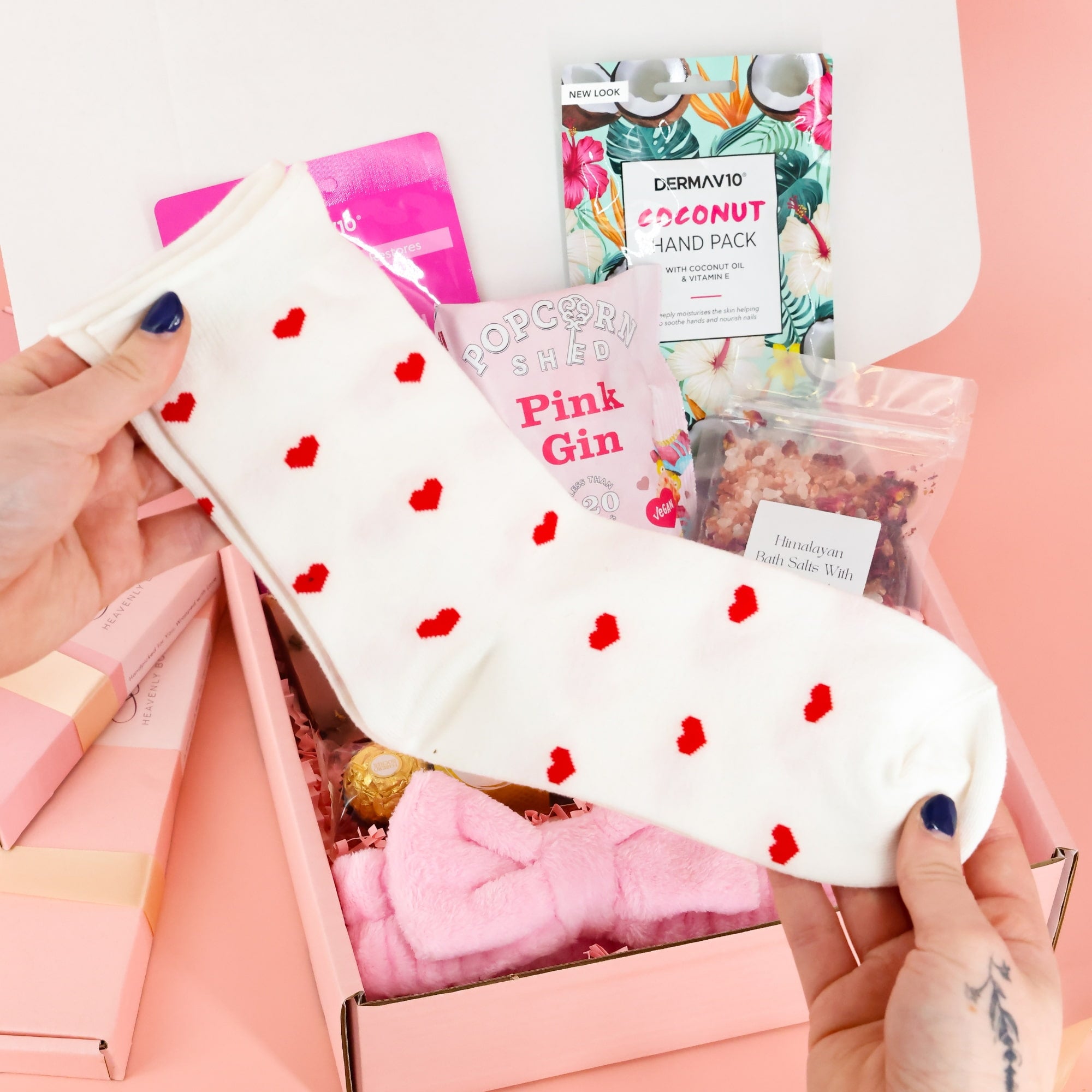 White crew socks with red heart patterns being held up, a cozy addition to a letterbox-friendly pamper gift box.