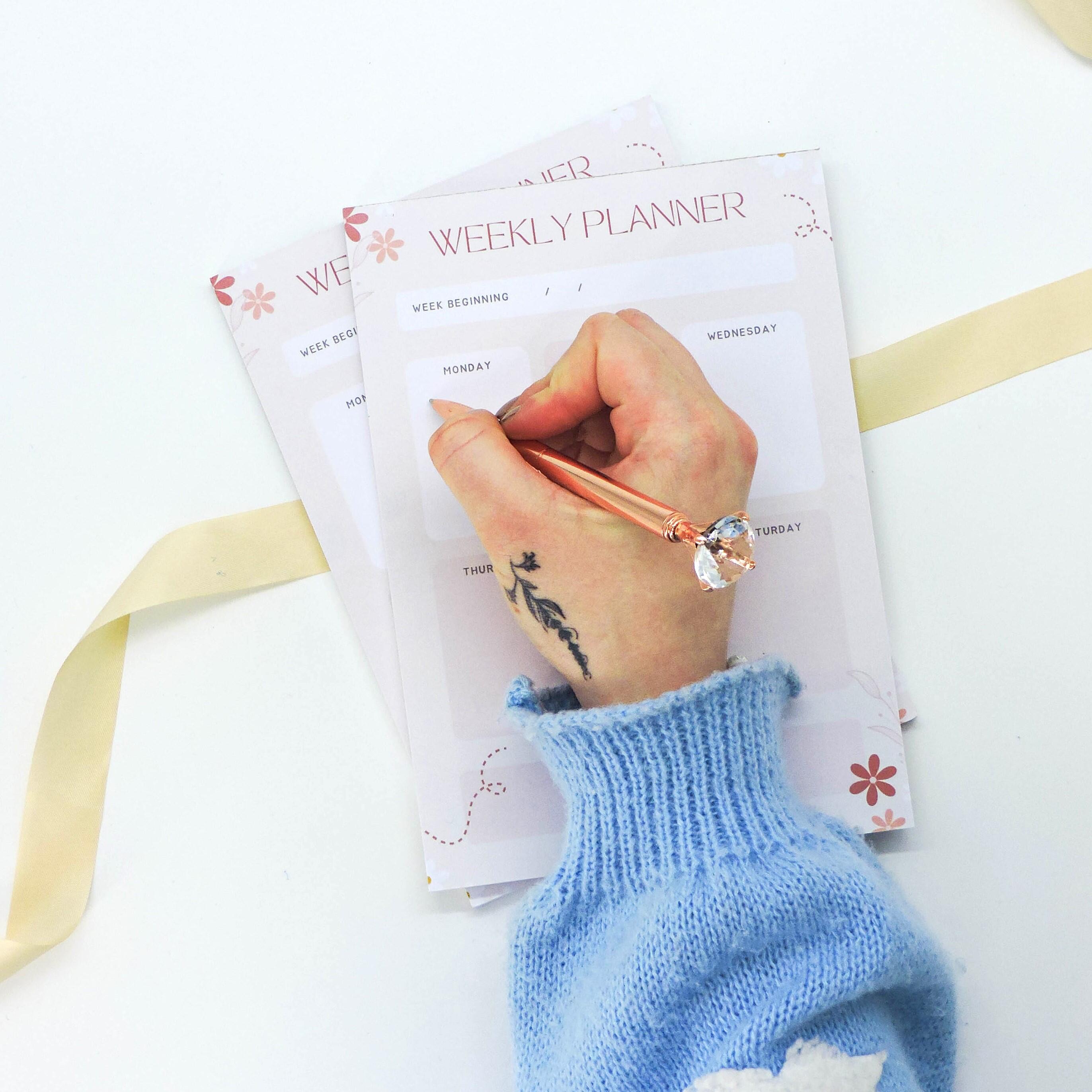 Hand holding a pen over the Weekly Planner - A5 Deskpad, showcasing its spacious sections for organizing tasks, priorities, and notes efficiently.