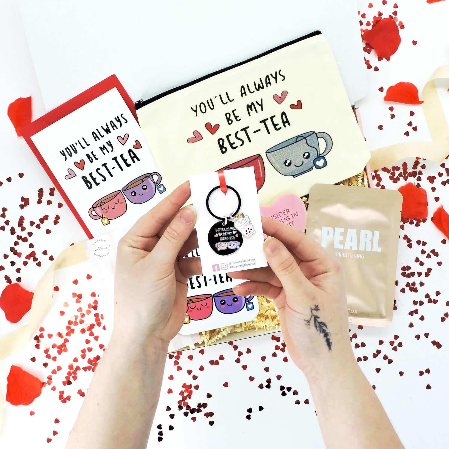 Hand holding a Best-Tea card from the Be My Best-Tea Gift Box for Valentine’s, featuring thoughtful goodies like a tote bag and Prosecco gummies.