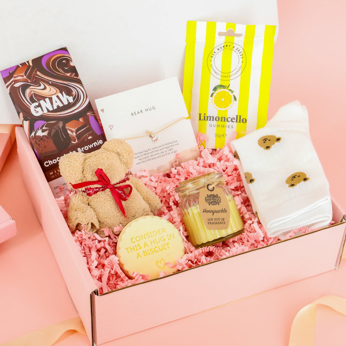 Bear Hug in a Box care package for self-care featuring a plush teddy bear, "hug in a biscuit" cookie, Gnaw chocolate, and cozy bear-print socks.