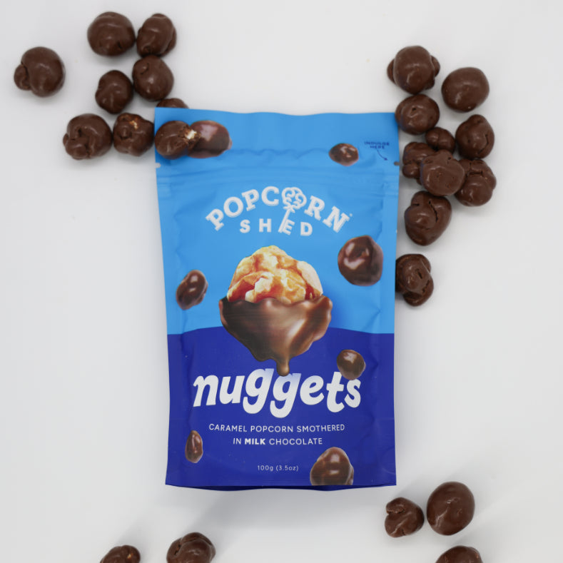 Popcorn Shed Chocolate-covered Caramel Popcorn: Close-up of popcorn coated in milk chocolate, bag showing popcorn bowl image, ideal indulgence for gifting, sharing, or personal treat.