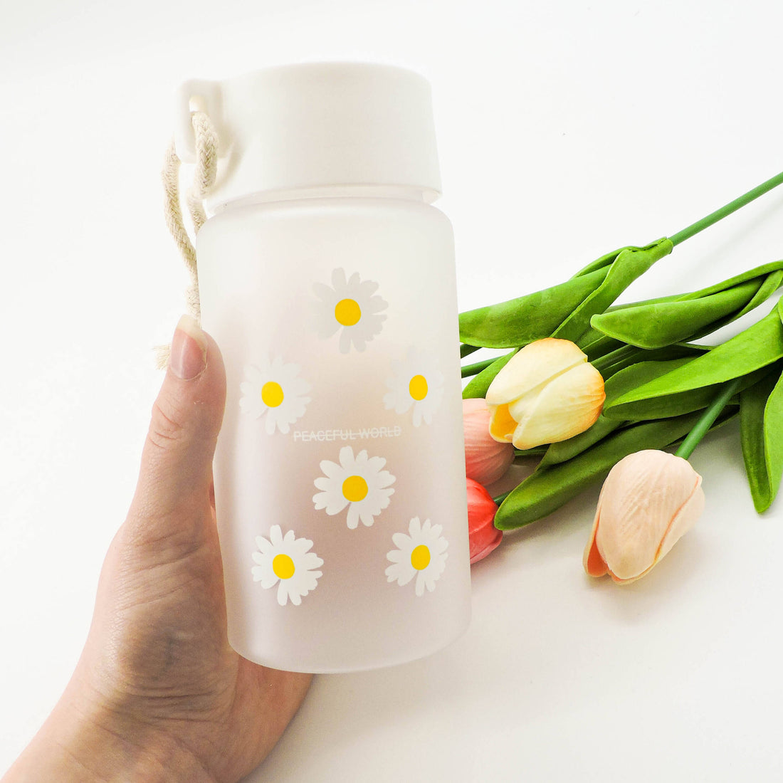Daisy Water Bottle held in hand, features daisy print on glass, secure lid, and rope handle for eco-friendly, stylish hydration.