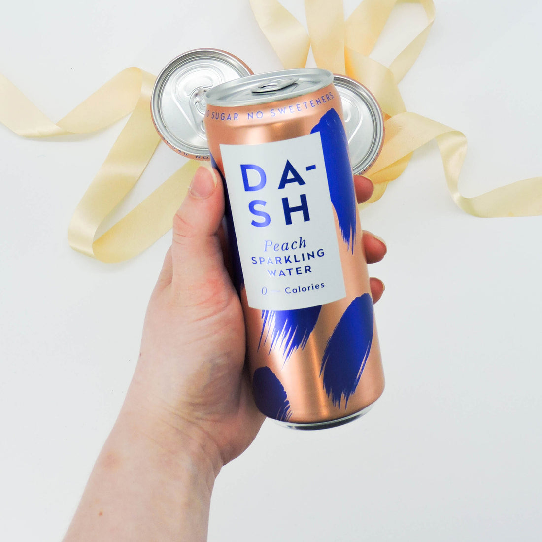 Dash Peach Sparkling Water can held by a hand, showcasing its sleek design. A refreshing, sugar-free beverage infused with real fruit flavor.