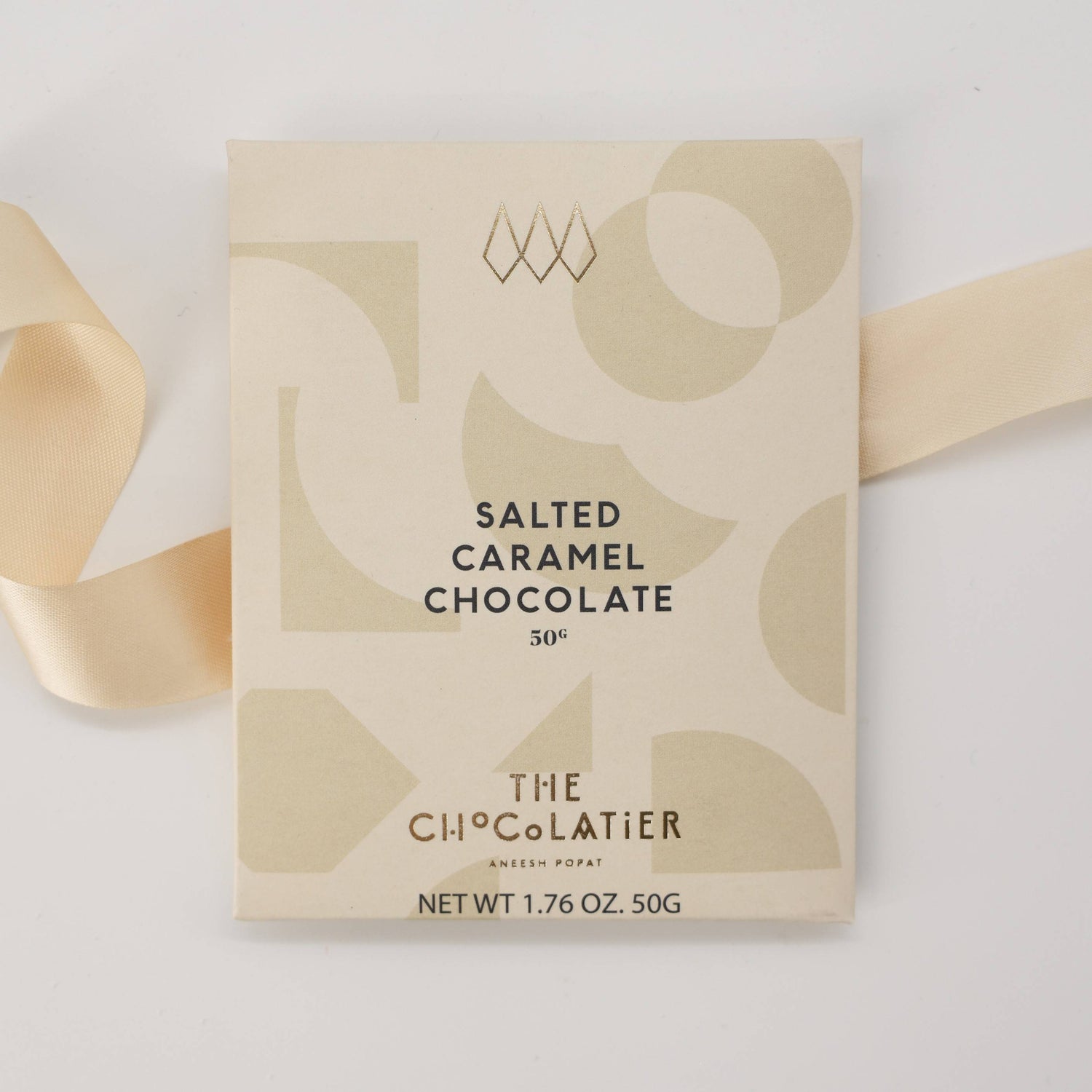The Chocolatier Salted Caramel Chocolate bar in elegant cream packaging with abstract shapes and pale gold ribbon, perfect for gifting and indulgence.