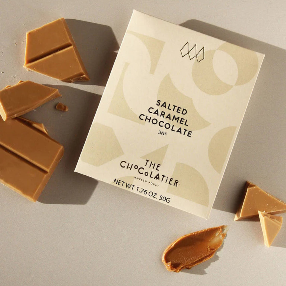 The Chocolatier Salted Caramel Chocolate bar in elegant cream packaging with abstract shapes and pale gold ribbon, perfect for gifting and indulgence.