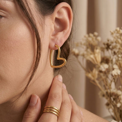 Minimalist 18k gold-plated heart-shaped hoop earrings for women, styled in a lifestyle photoshoot with matching gold stackable rings and a neutral, bohemian background.