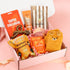 Overhead view of a "Hug in a Box" care package for women featuring butterscotch popcorn, Pukka ginger tea, a collagen mask, Sanctuary Spa cream, and cute teddy bear socks.