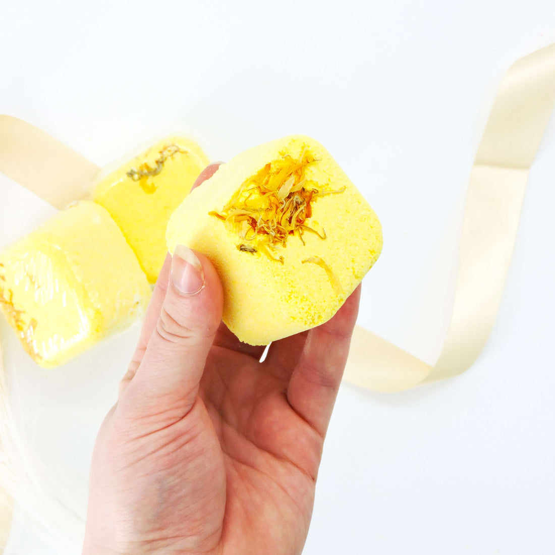 Hand holds Aromatherapy Shower Steamer - Spearmint, Lemon, Eucalyptus &amp; Calendula Flowers, capturing its compact, spherical shape, ideal for energizing shower experiences.
