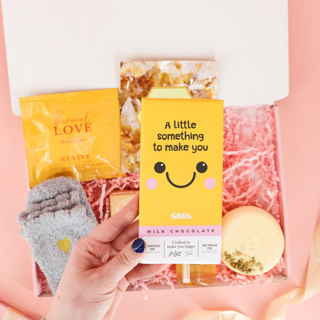 Hand holding a yellow Gnaw milk chocolate bar featuring a smiley face and the text "A little something to make you smile," included in a positive mental health care package.