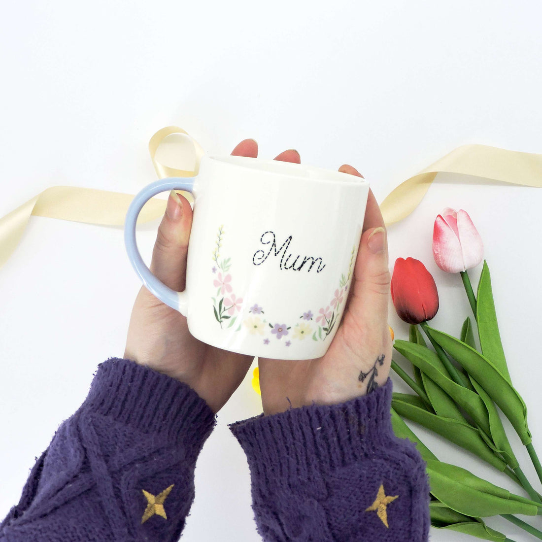 Mum Ceramic Mug - Floral Design, featuring a close-up of a delicate flower pattern and a pastel blue handle, showcased on a table.