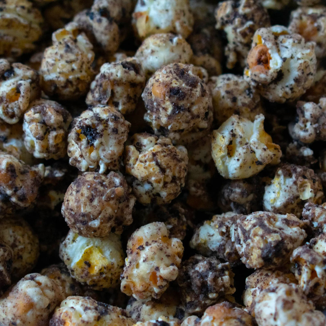 Cookies &amp; Cream Popcorn; close-up of white chocolate caramel popcorn with cookie crumbs, highlighting a vegan, all-natural snack, emphasizing creamy and sweet indulgence.