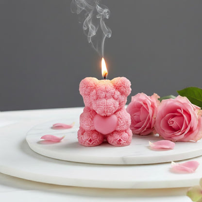 Lit pink rose bear scented candle shaped like a teddy bear made of roses, displayed on a marble tray with fresh pink rose petals for a romantic gift setting.