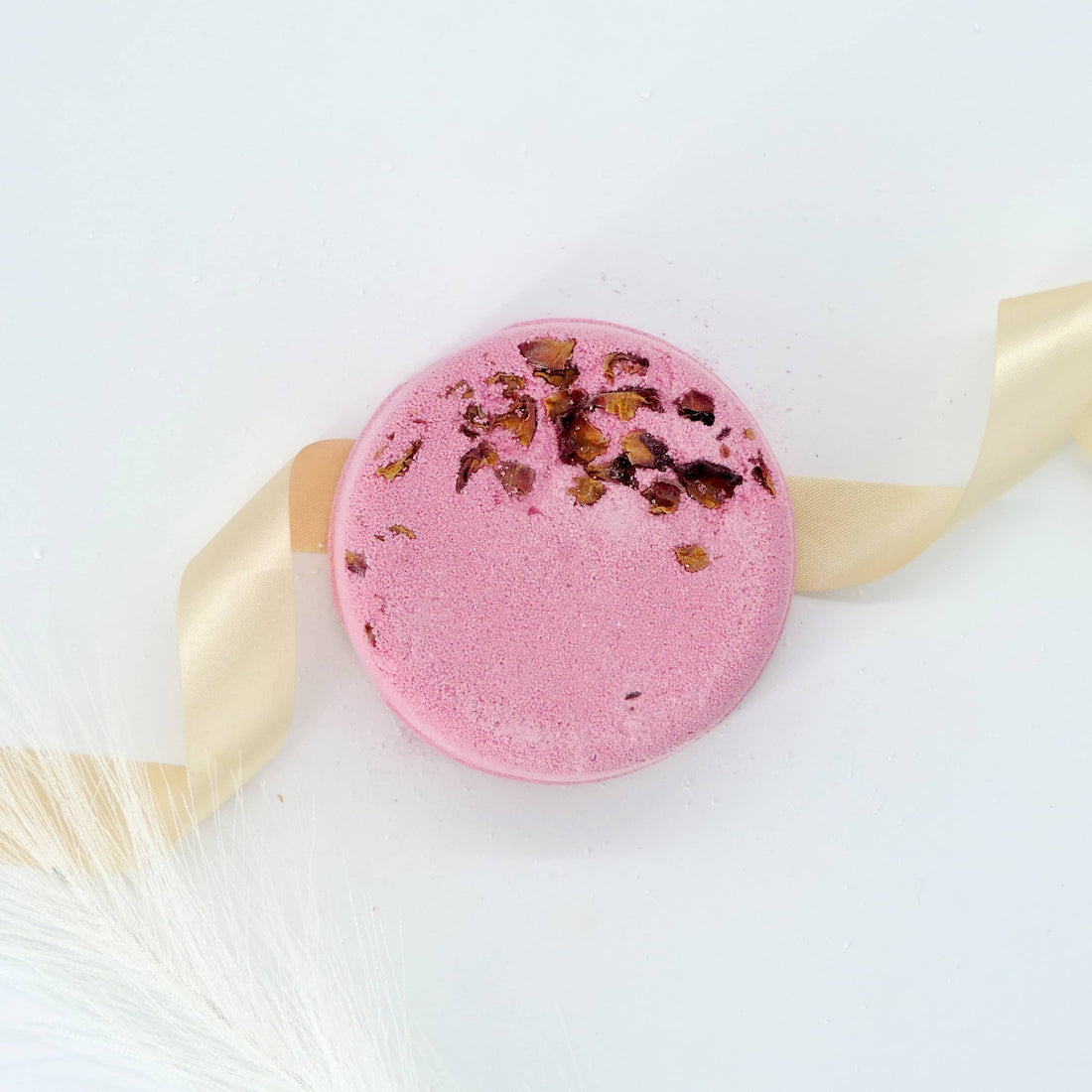 Rose, Lavender, Patchouli Bath Bomb with a gold ribbon, shaped like a pink macaroon, offering relaxation and tension relief.