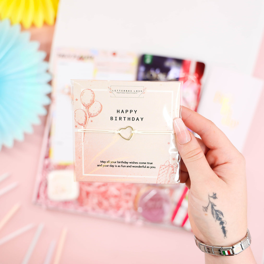 Self-Care Birthday Pamper Set by Heavenly Boxes – close-up of “Happy Birthday” wish bracelet with heart charm on pink card; thoughtful birthday gift for her.