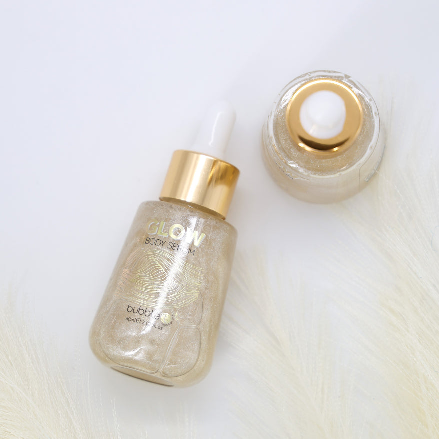 Glow Shimmer Body Serum bottle close-up, highlighting its gold cylinder design, emphasizing its lightweight, hydrating formula that adds a subtle, radiant shimmer to the skin.
