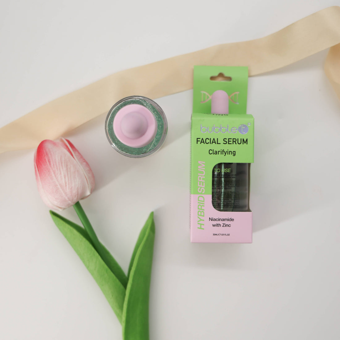 Bubble T Clarifying Facial Serum with niacinamide and zinc, in a box and dropper-top bottle, styled with a tulip and ribbon.