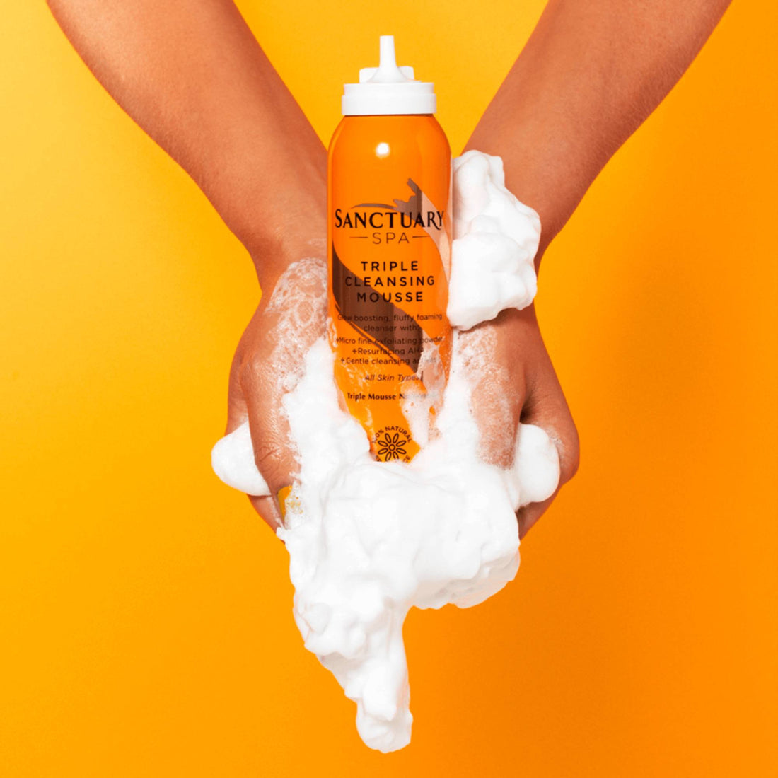 Person holding Sanctuary Spa Triple Cleansing Mousse bottle, showcasing its foamy texture, highlighting its exfoliating and cleansing properties for daily skincare routine.
