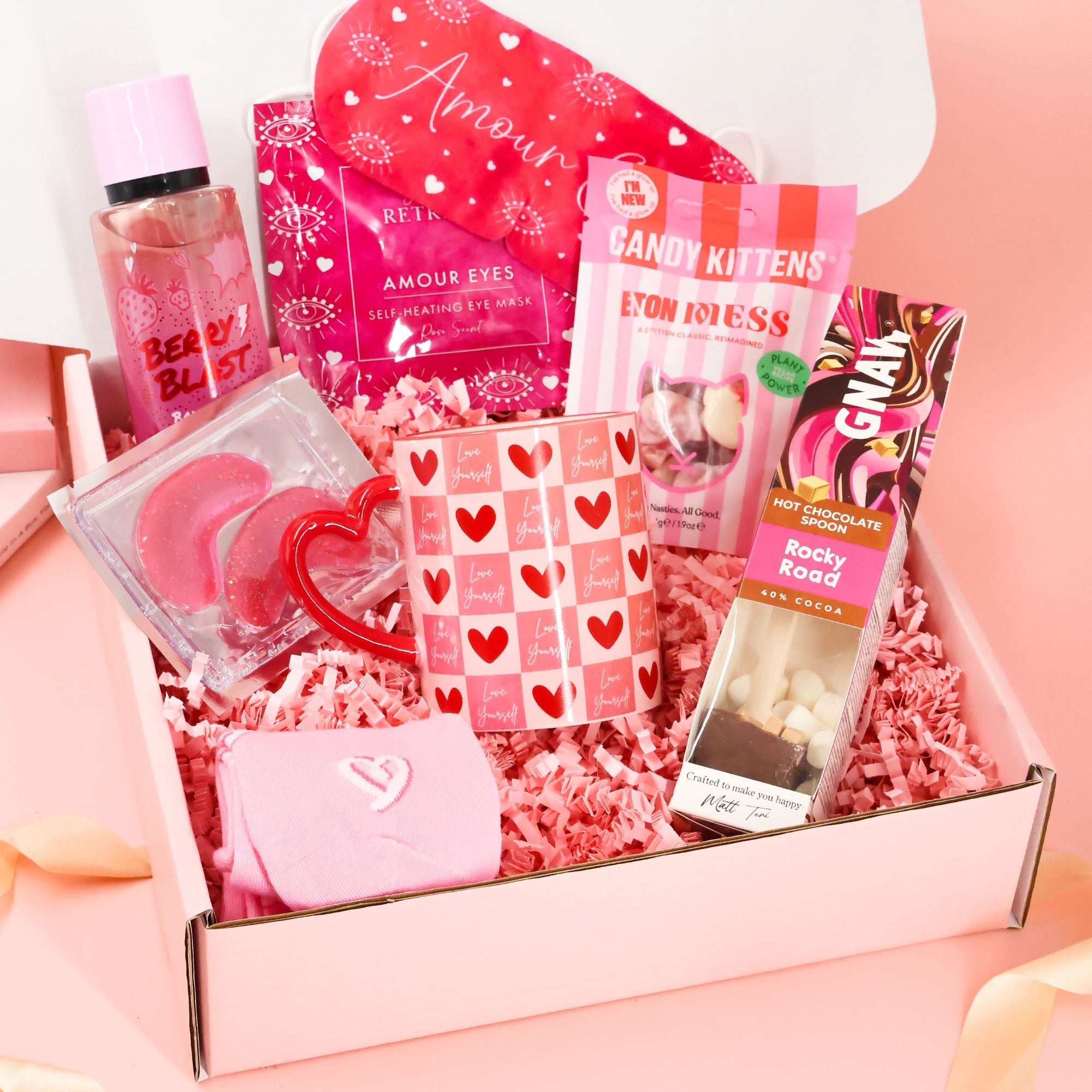 Ultimate pink self-care care package featuring a "Love Yourself" heart mug, Berry Blast body mist, Candy Kittens, and a Rocky Road hot chocolate spoon in a pamper gift box.