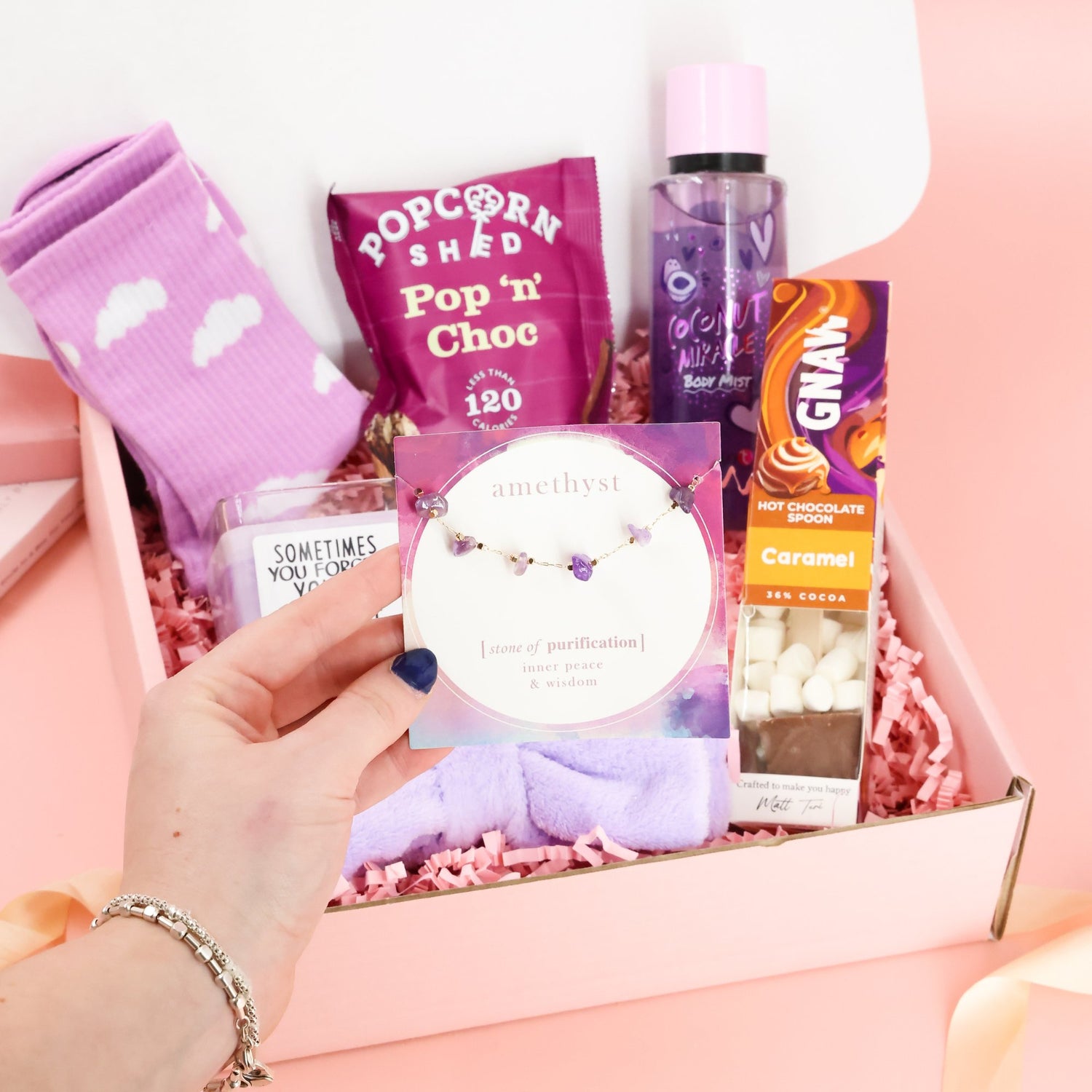 Amethyst "stone of purification" bracelet held in front of a luxury self-care pamper box gift set.
