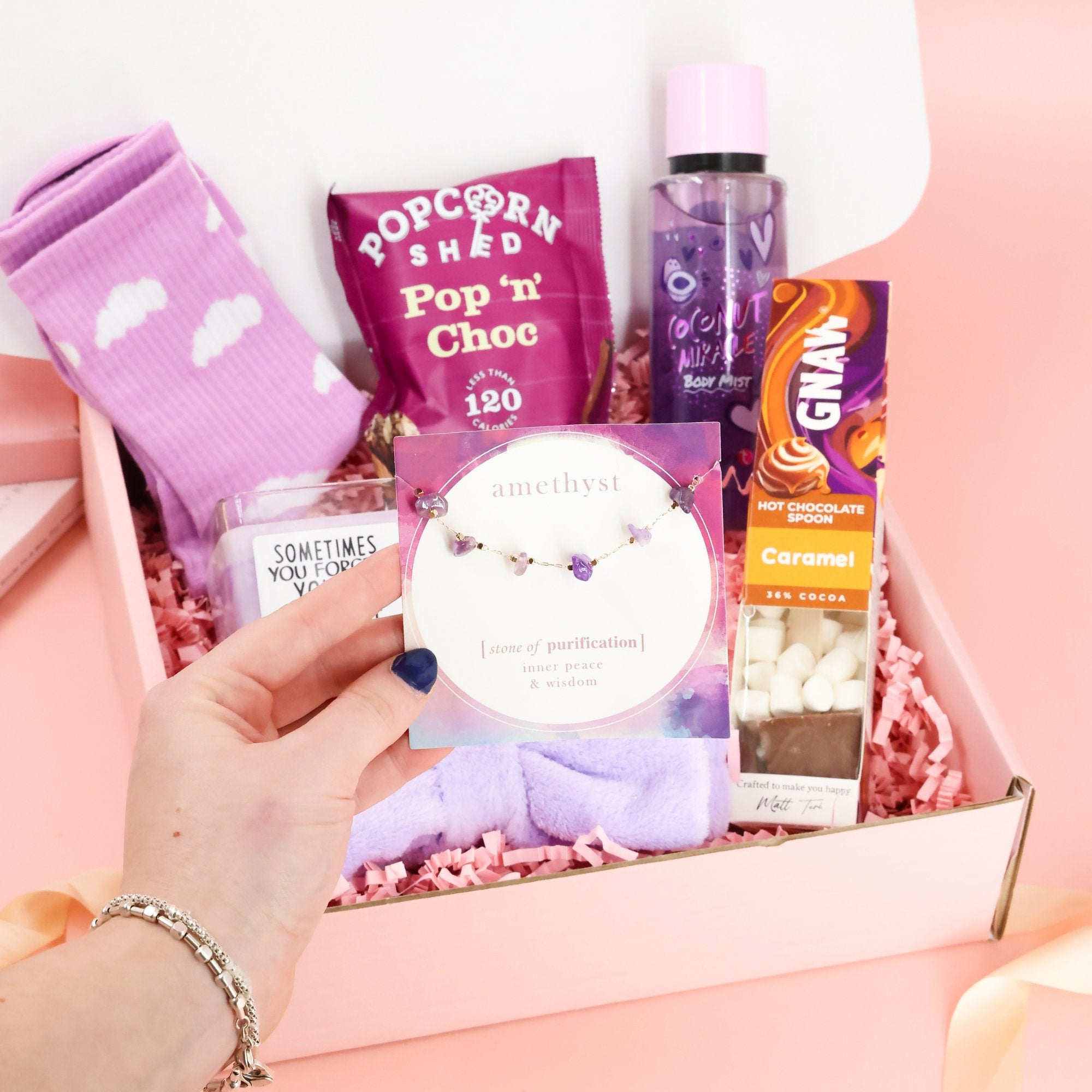 Amethyst "stone of purification" bracelet held in front of a luxury self-care pamper box gift set.